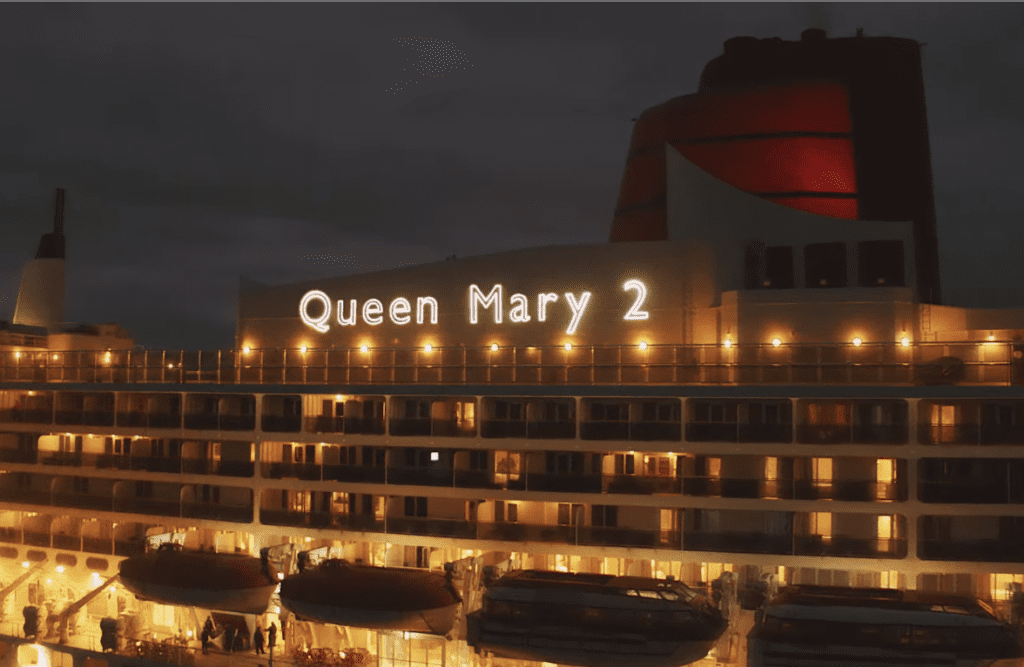 The queen mary 2 is lit up at night.
