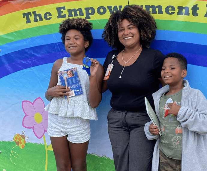 A woman and two children stand in front of a banner that says the Pawtucket Arts Festival's empowerment fund.