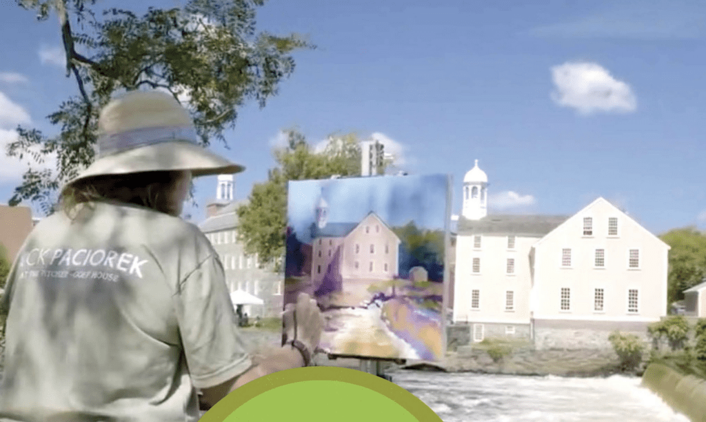 A woman in a hat is creating art in front of a river.