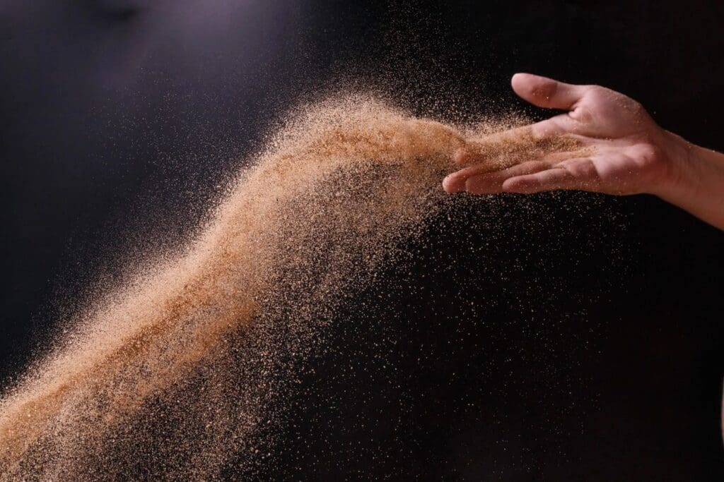 A person's hand is throwing sand onto a black background.