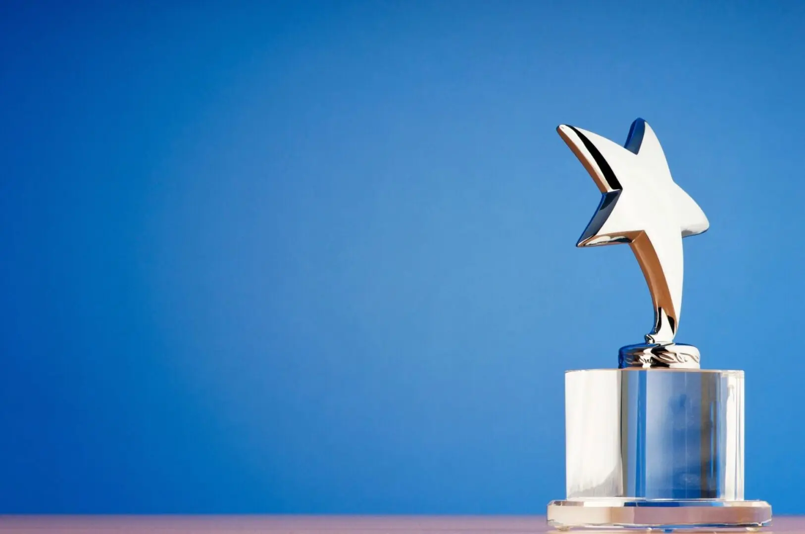 A silver star trophy on a table against a blue background.