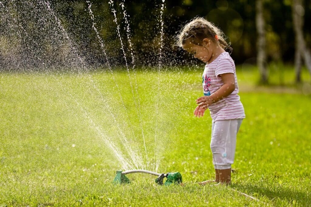 A little girl playing with a sprinkler in the grass.