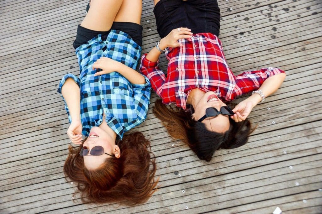 Two young women laying on a wooden deck.
