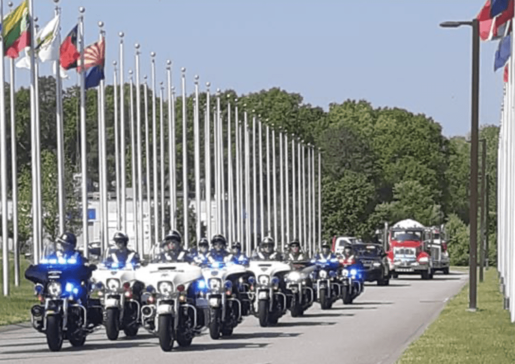 A group of police officers riding motorcycles down a street with flags, forming a motorcycle convoy.
