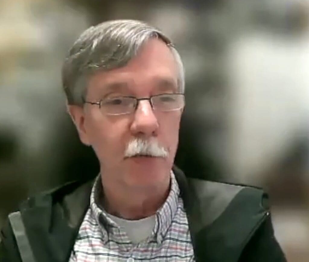 A homeless man with glasses and a mustache is talking.
