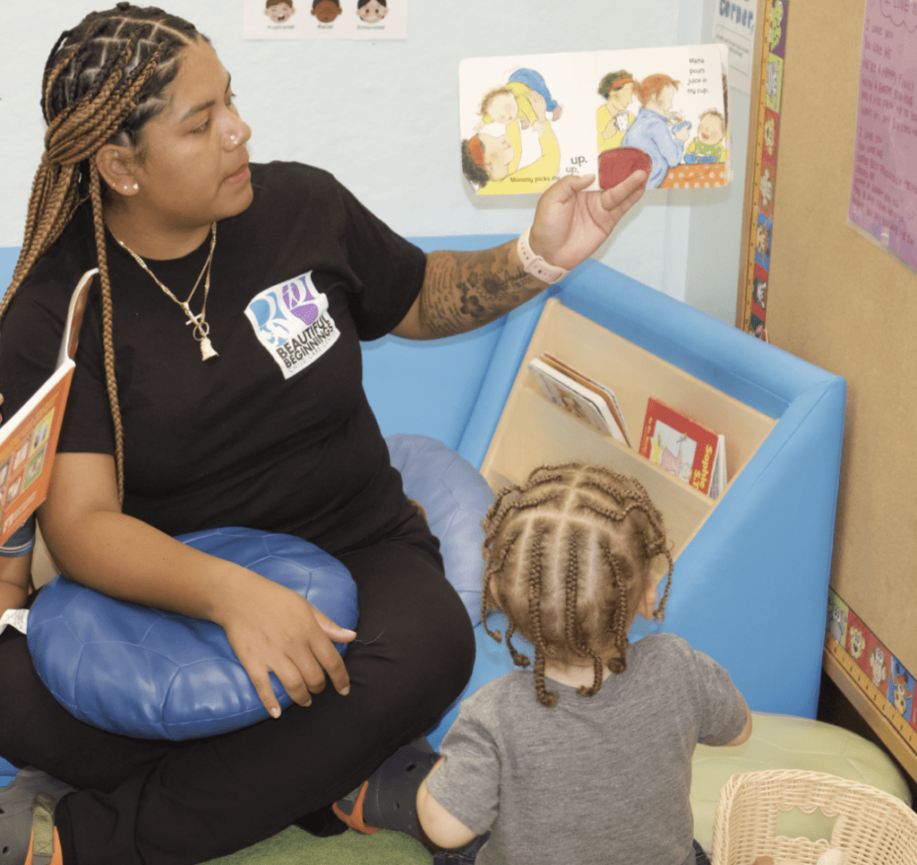 A woman providing food assistance to a child in a classroom while reading to them.