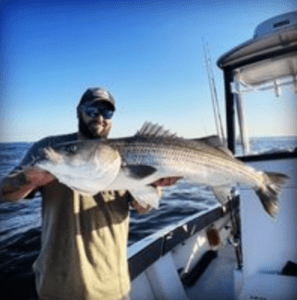 A man holding up a striped bass on a boat.