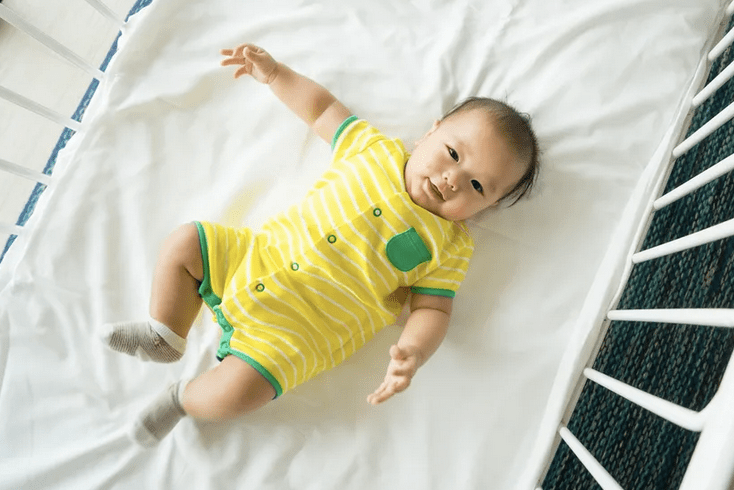 In honor of Baby Safety Month, a precious baby peacefully rests in a yellow striped shirt within the safety of a crib.