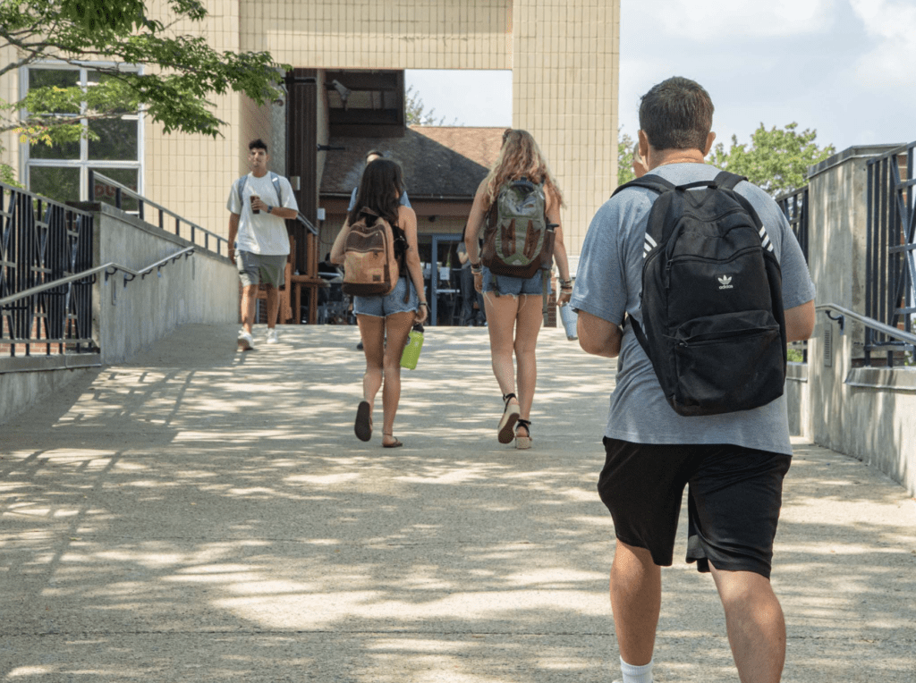 A group of URI students walking down a sidewalk with backpacks.
