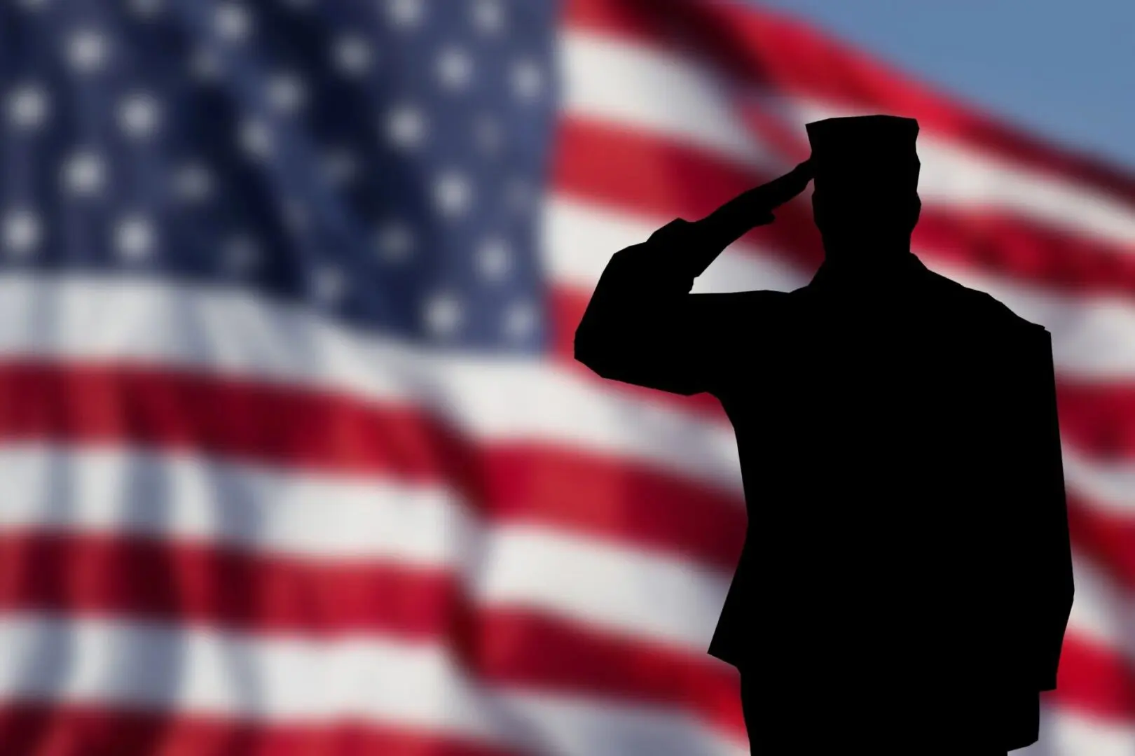 A silhouette of a soldier saluting in front of an american flag.