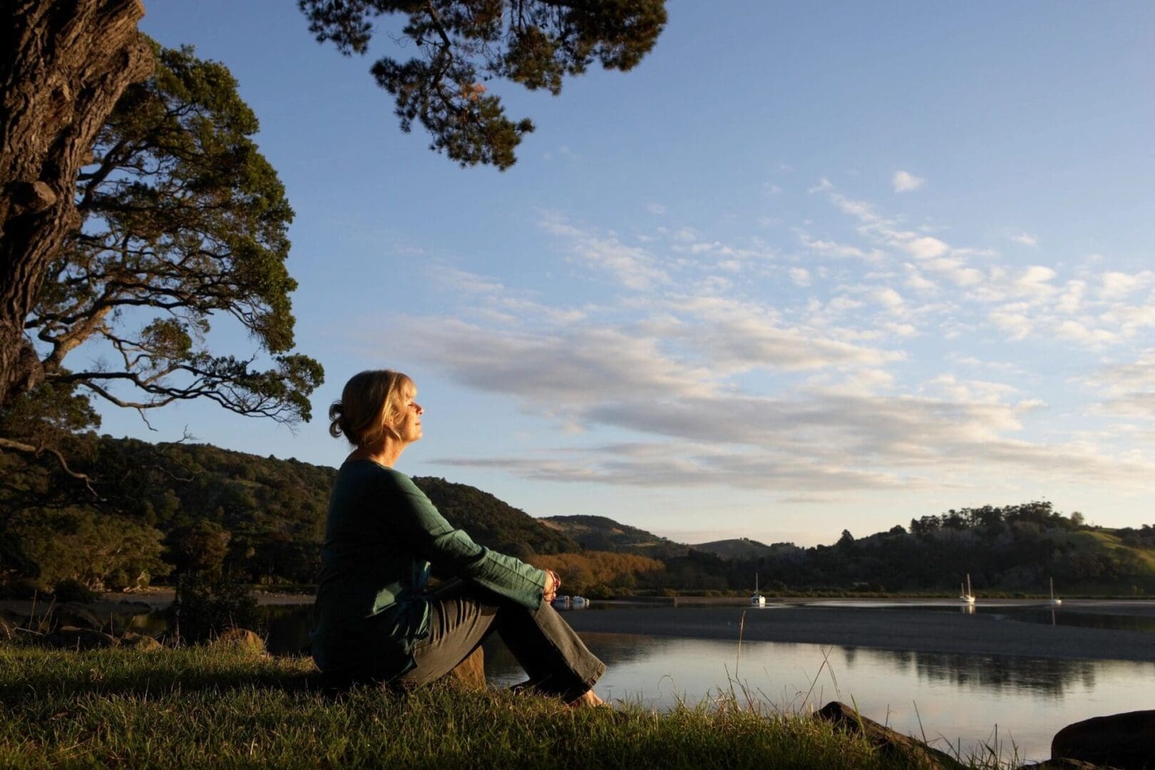 A woman sits on a rock overlooking a lake.