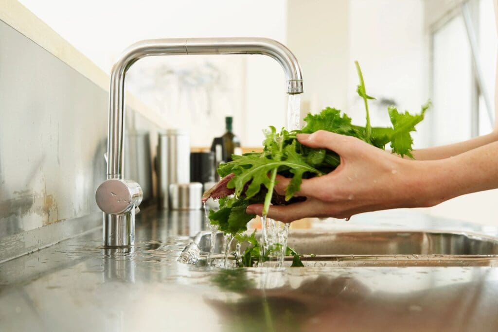 A person is washing greens in a kitchen sink.