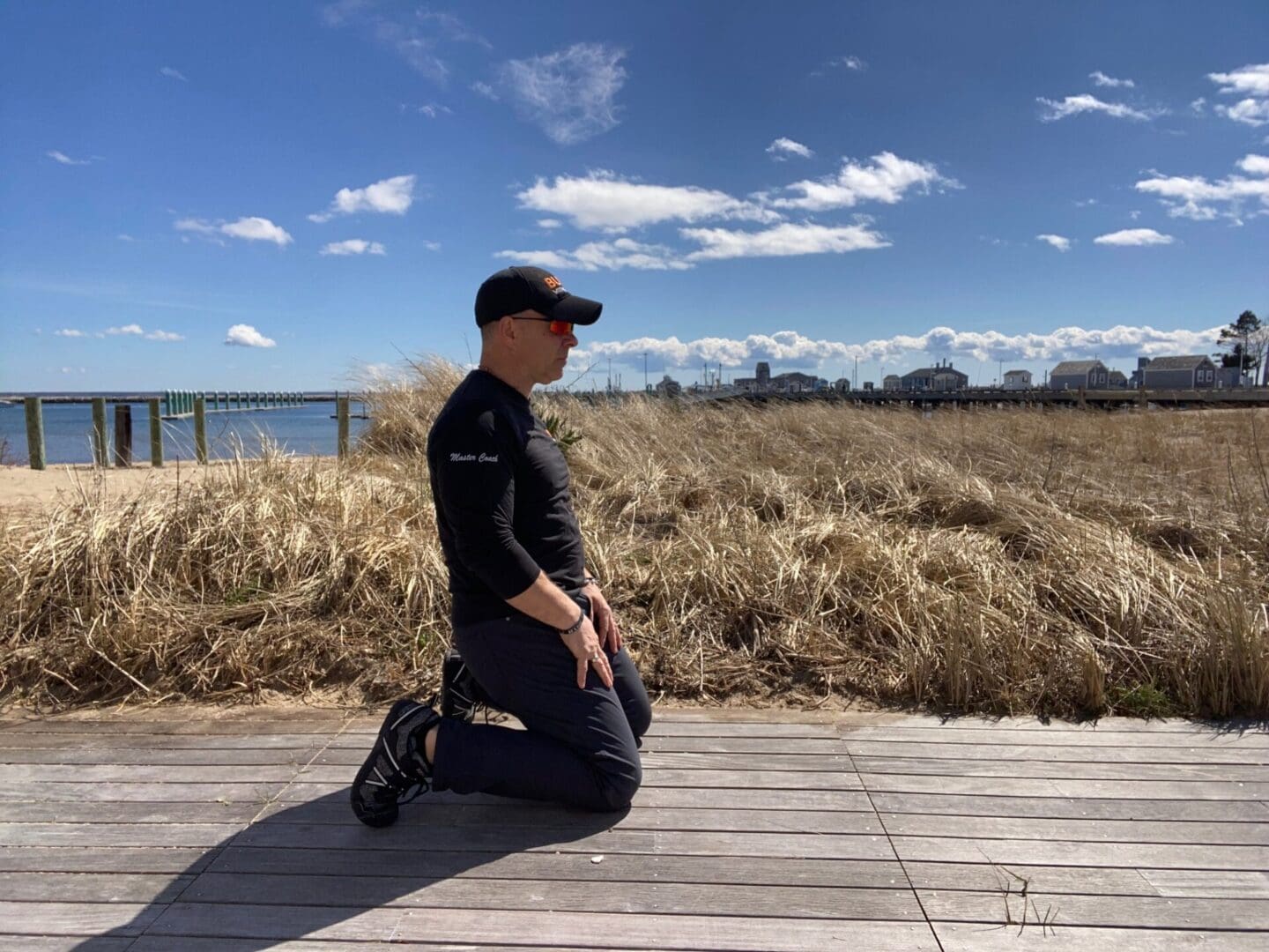 A man exercising, kneeling on a boardwalk next to a body of water.
