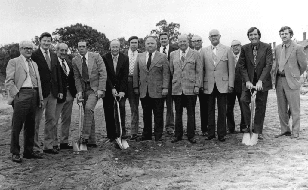 A group of men standing in a fore court with shovels.