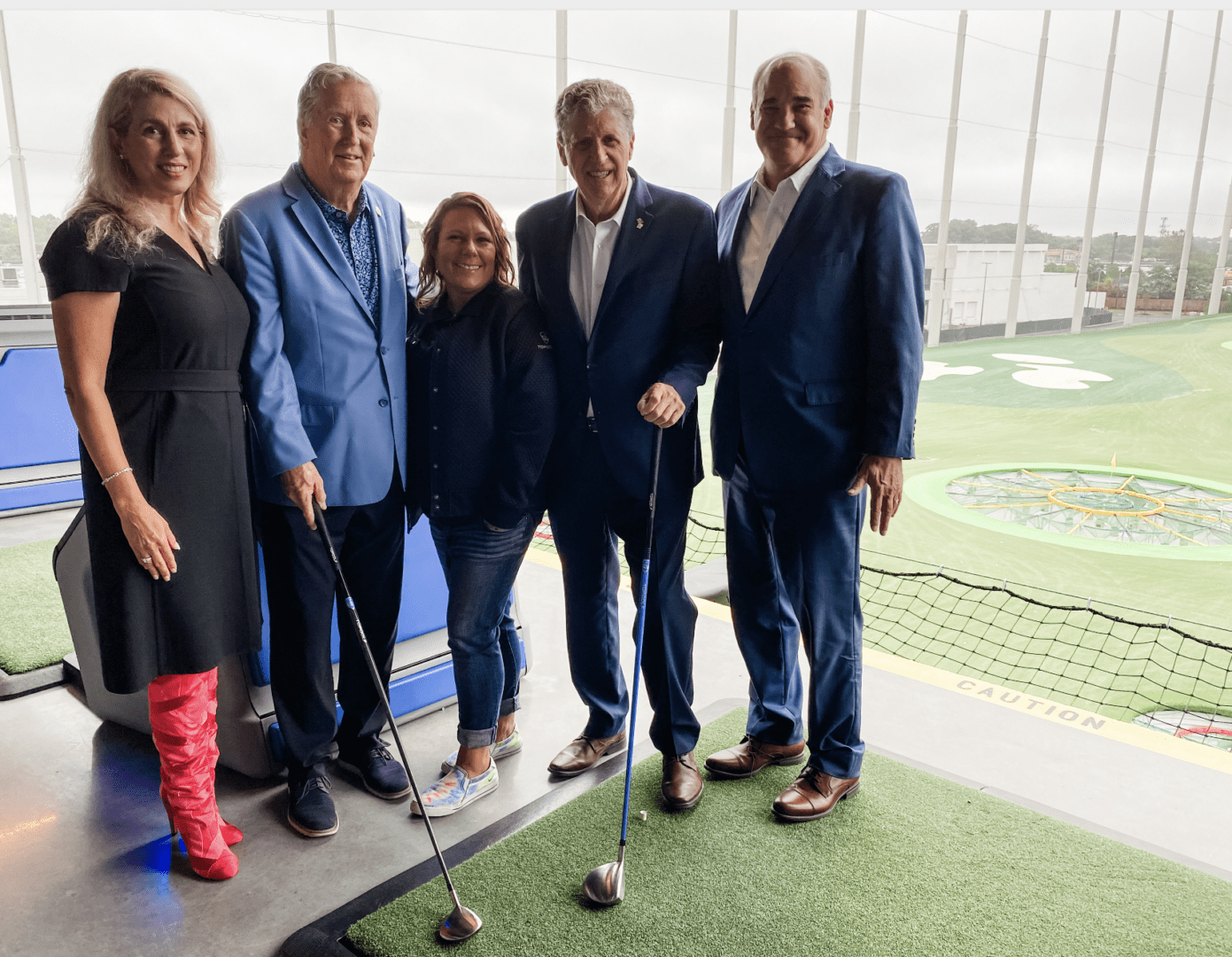 A group of people posing for a picture in front of a TopGolf course.