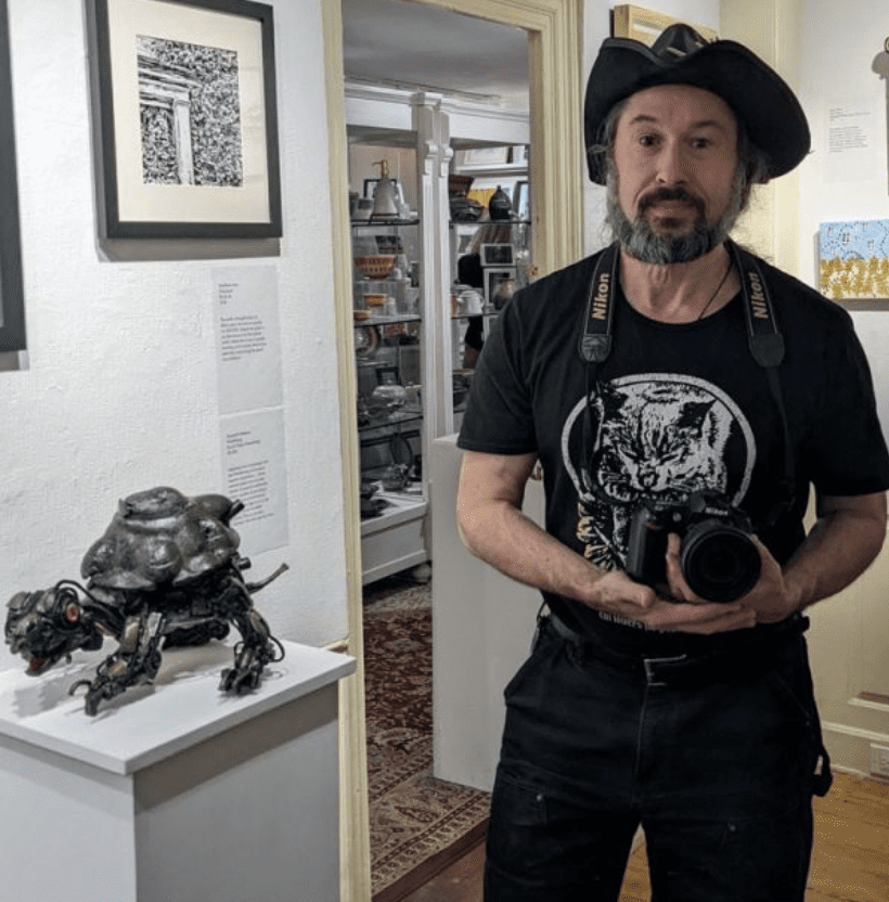 A man in a pirate hat is capturing an art sculpture in a photograph.