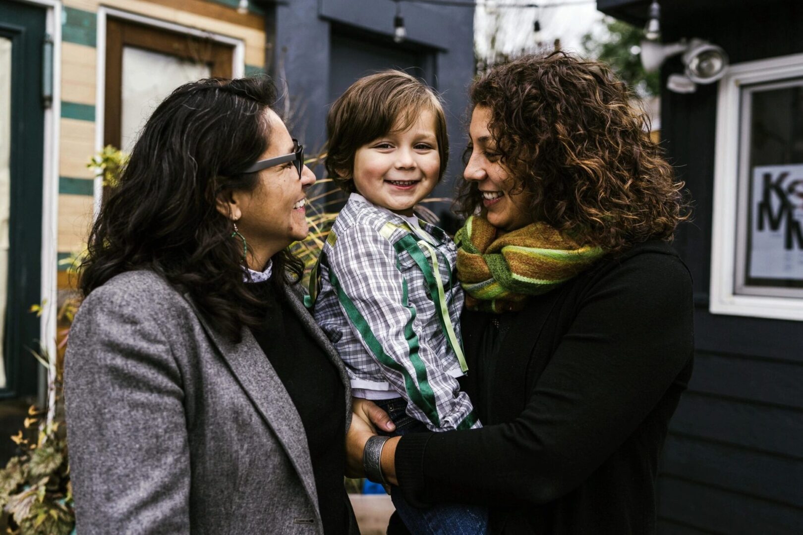 Two women holding a child in front of a house.