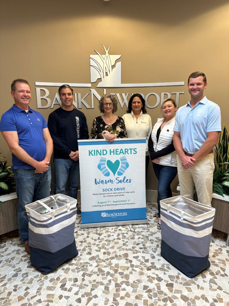 A group of people standing in front of a sign that says BankNewport and kind hearts.