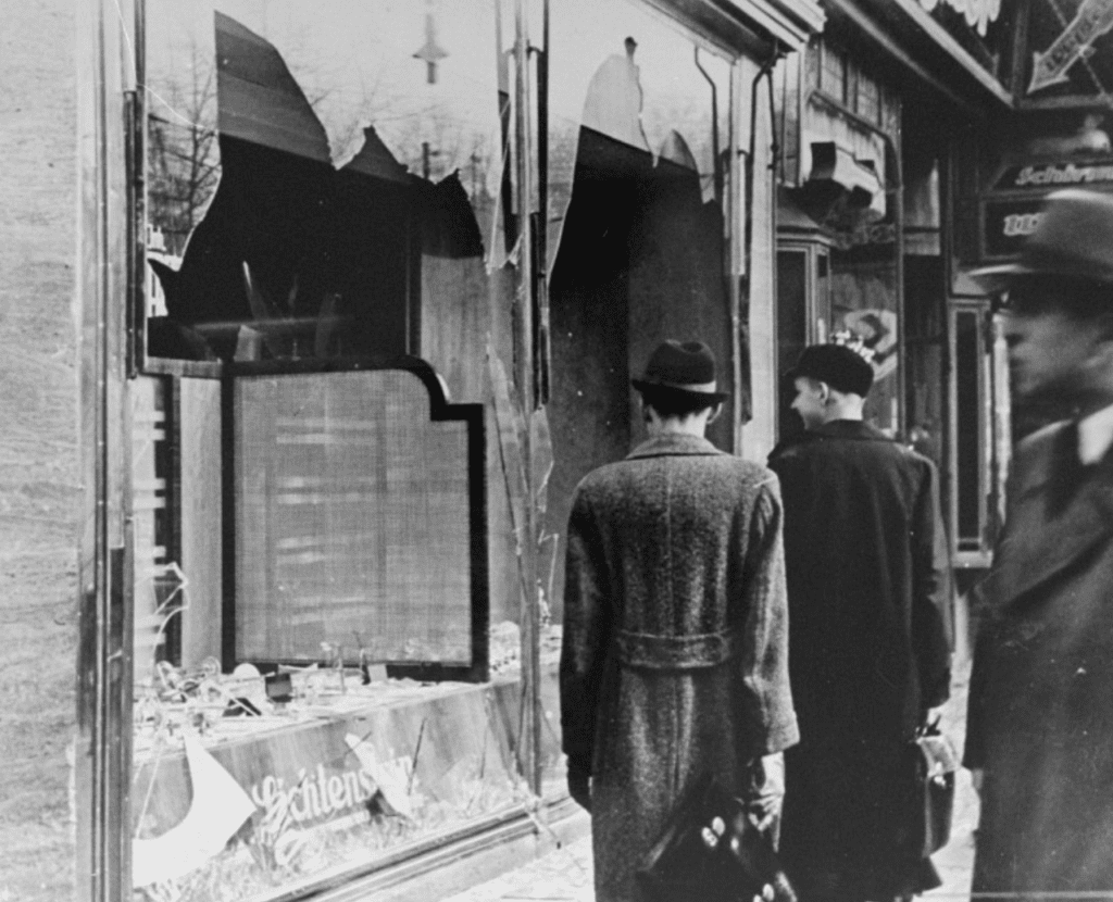 A group of people walking down a street during Kristallnacht with a broken window.
