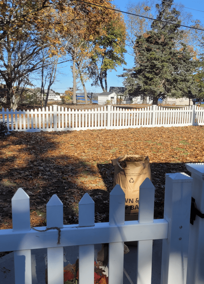 A white picket fence in a yard surrounded by leaves.