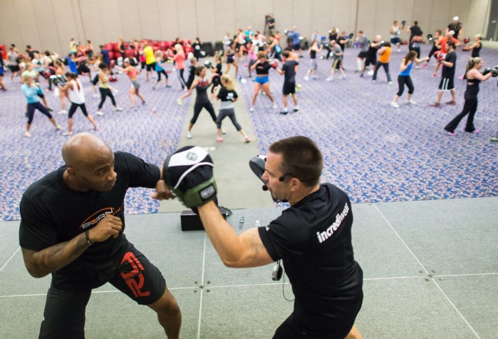 Two men engaged in a self-defense workout session at a gym.