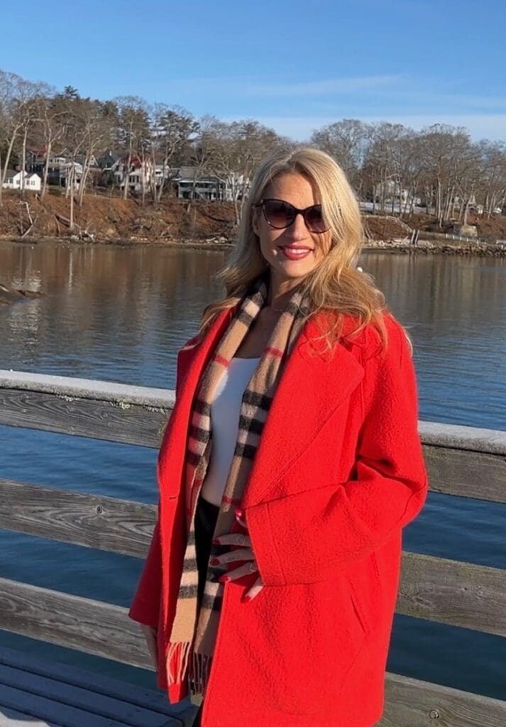 A woman in a red coat standing on a dock near real estate.