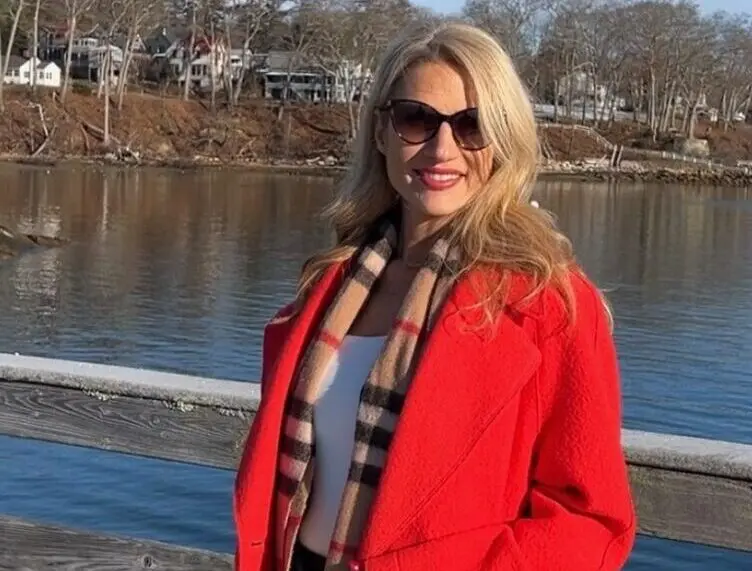 A woman in a red coat standing on a dock near real estate.