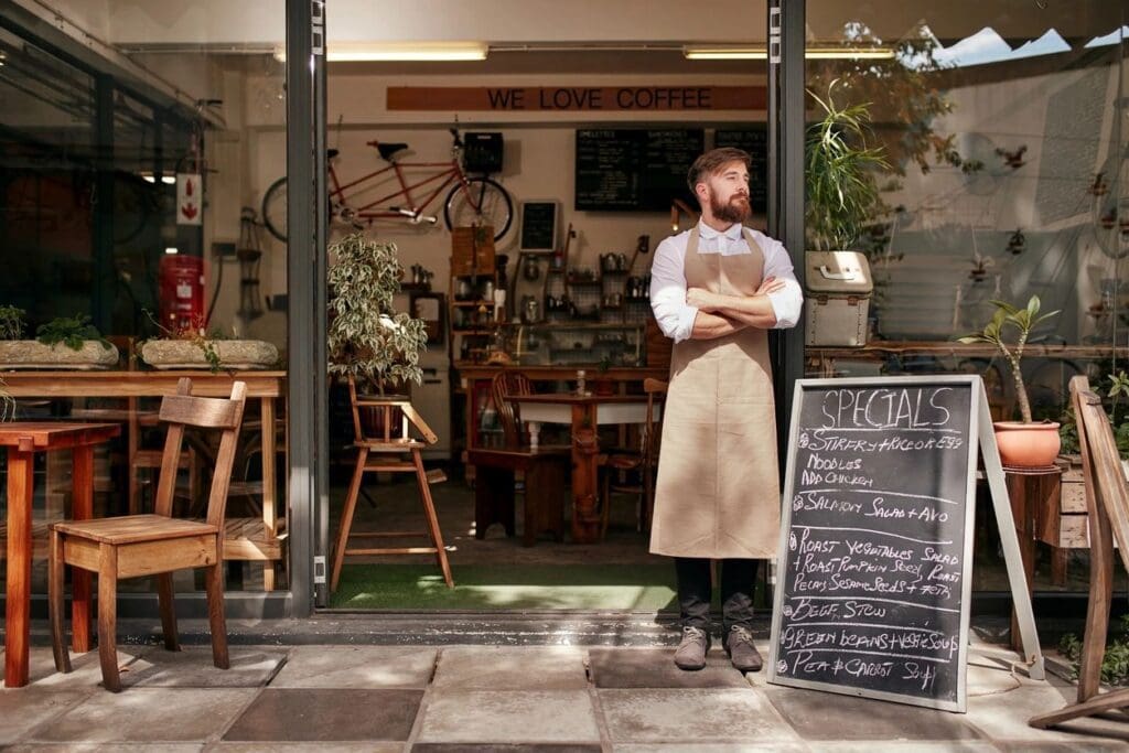 A man in an apron standing in front of a restaurant.