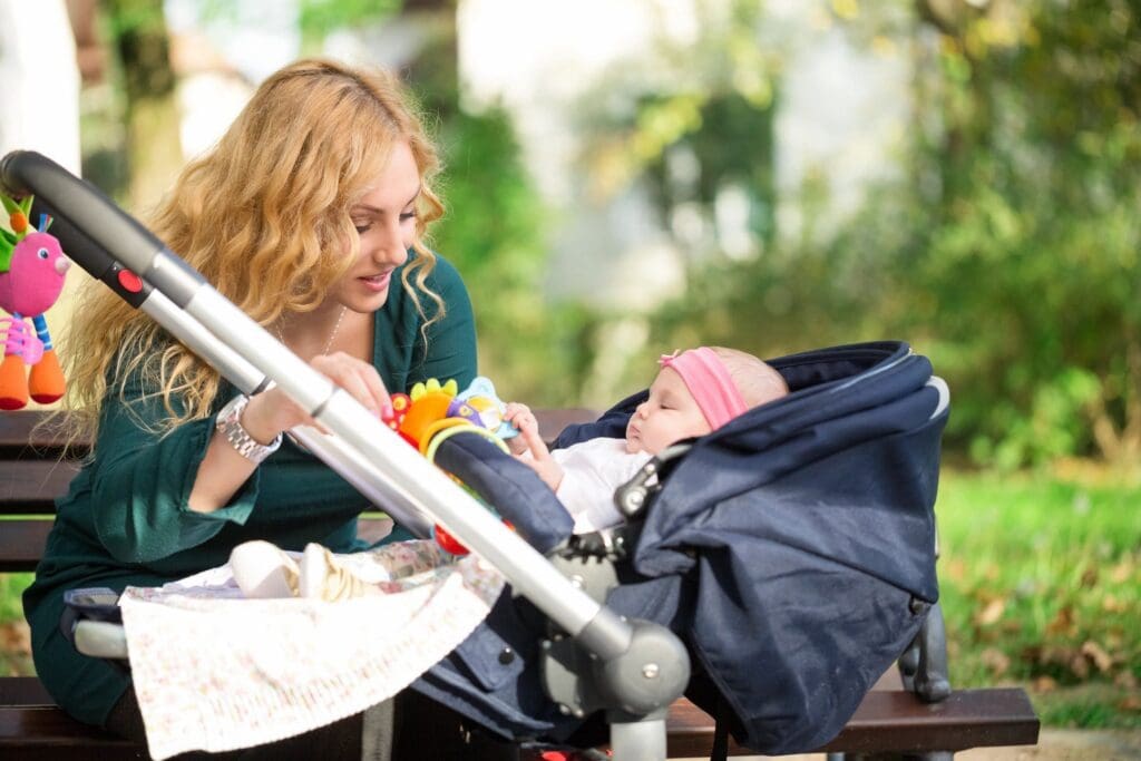 A woman is sitting on a bench with her baby in a stroller.