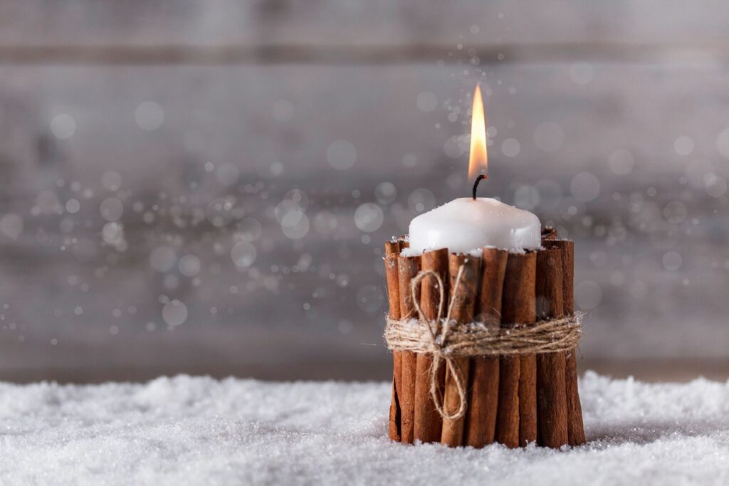 A candle with cinnamon sticks in the snow.