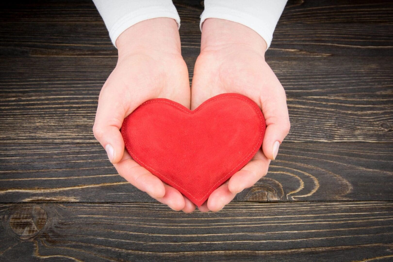 A woman's hands holding a red heart on a wooden table.