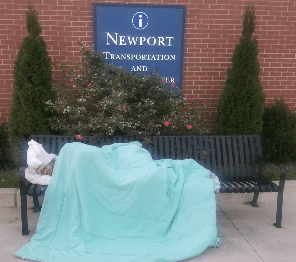 A homeless person sleeping on a bench in front of a building in RI.
