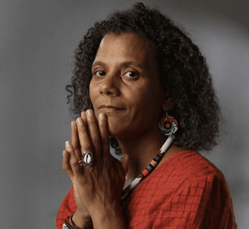 A woman with curly hair is captivated by black storytelling as she poses with her hands clasped.