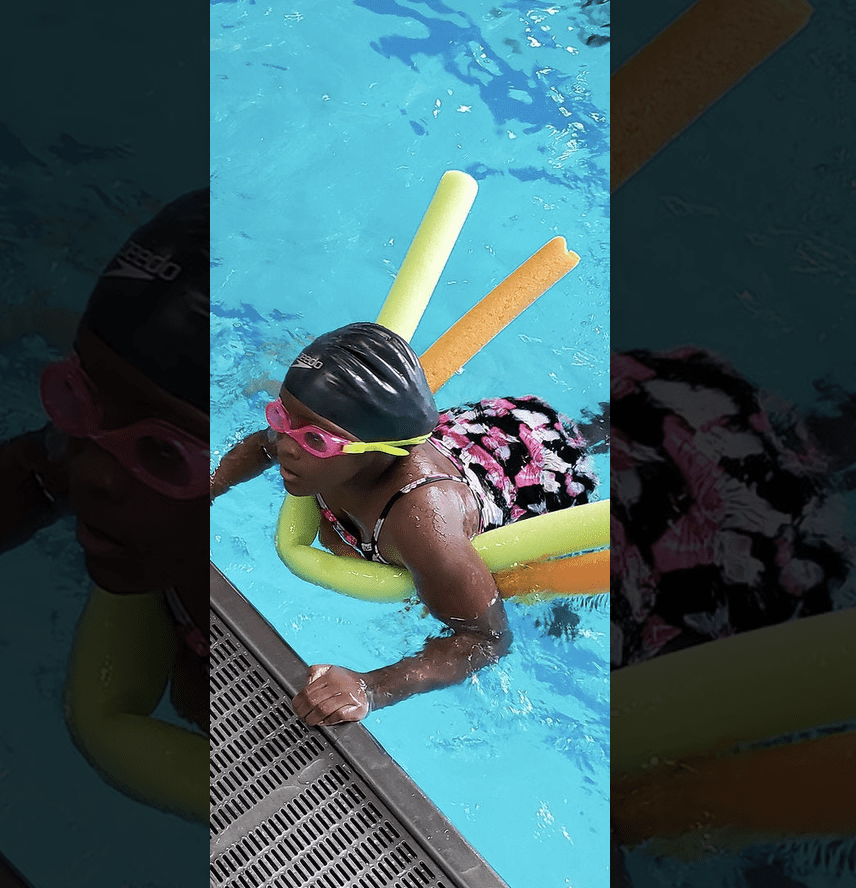 A girl swimming in a pool with goggles and floats.