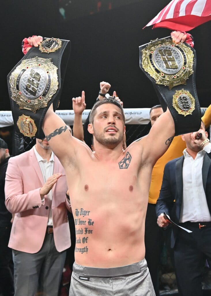 Gary Balletto, a man with tattoos, holding up his belts in front of a crowd.