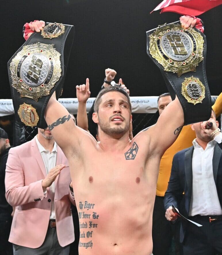 Gary Balletto, a man with tattoos, holding up his belts in front of a crowd.