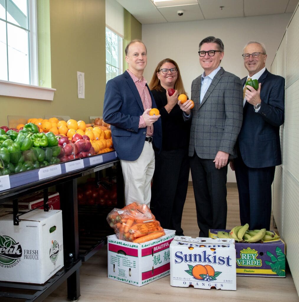 Four people standing in front of boxes of fruits and vegetables.