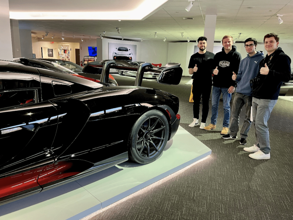 A group of men standing next to a black sports car in a car museum.