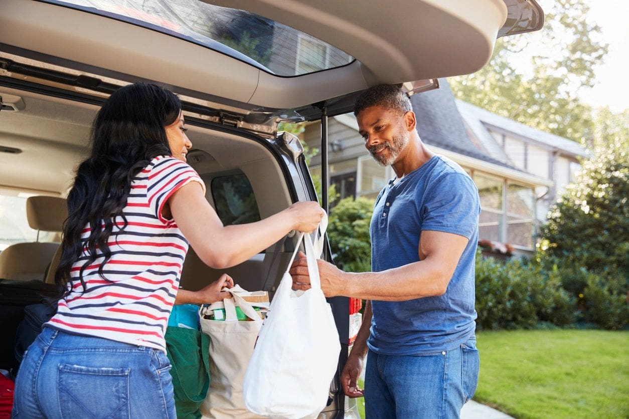 A man and woman putting groceries into the trunk of a car.