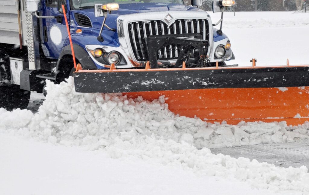 A snow plow driving down a snowy road.