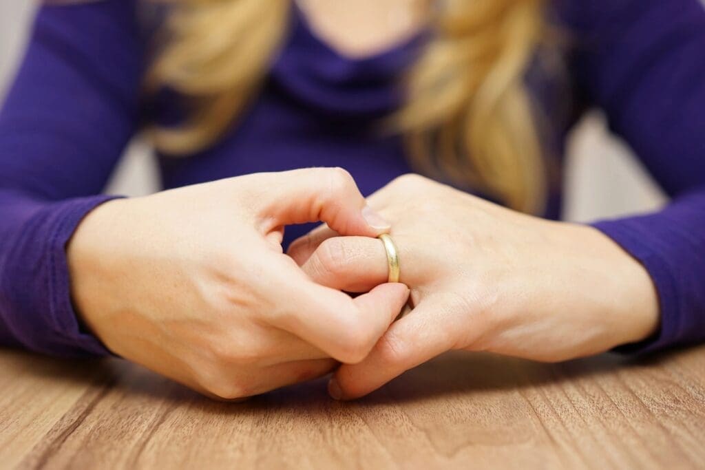A woman's hand holding a wedding ring on a table.