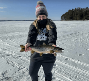 A woman holding up a brown trout outdoors on a frozen lake.