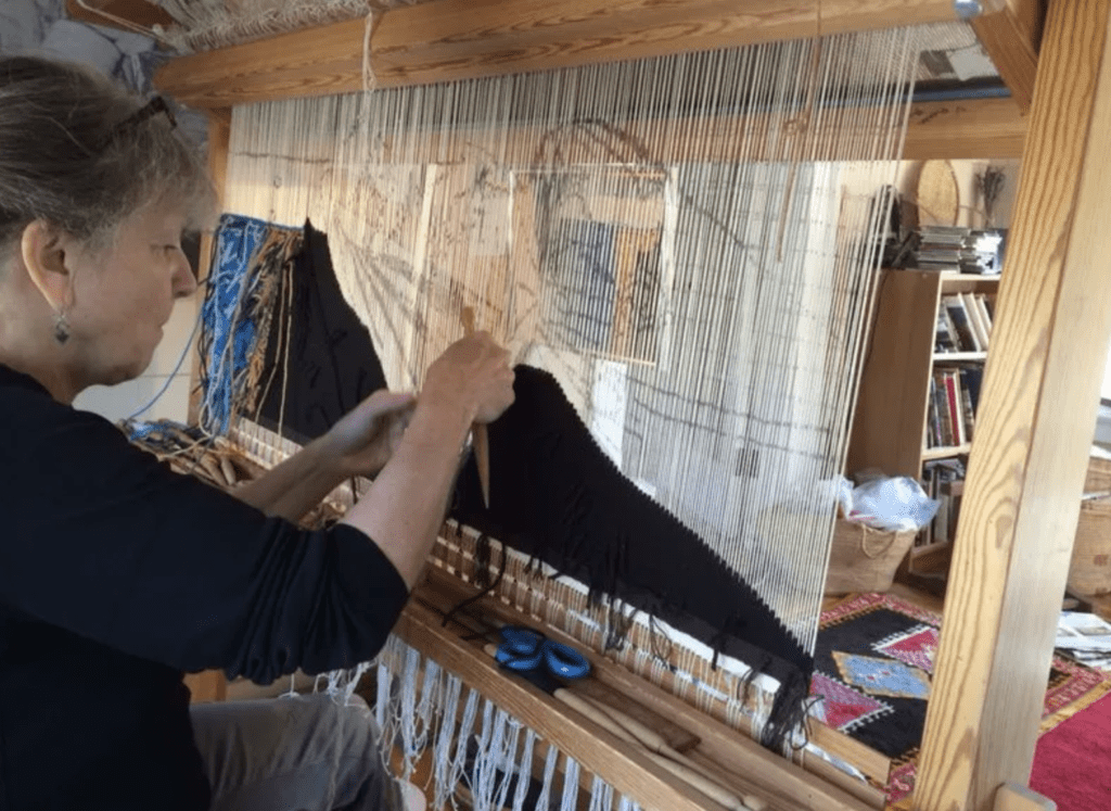 A woman is creating art on a wooden loom.