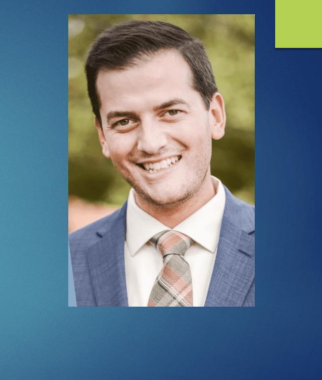 A man in a suit and tie smiles at the SBA Awards in front of a blue background.