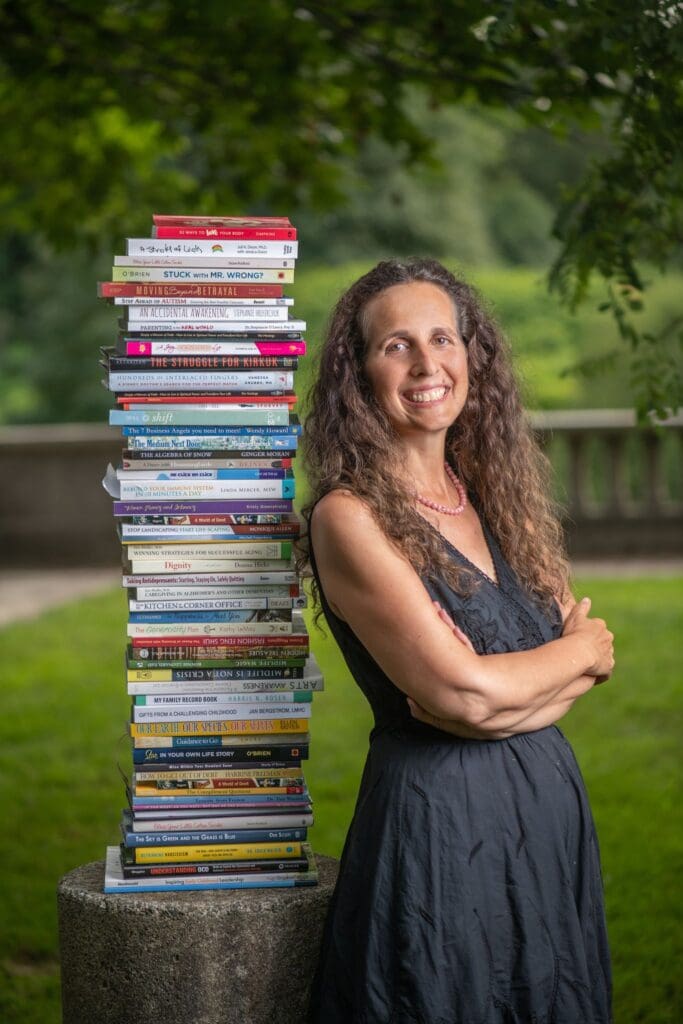 Woman standing with a stack of books.