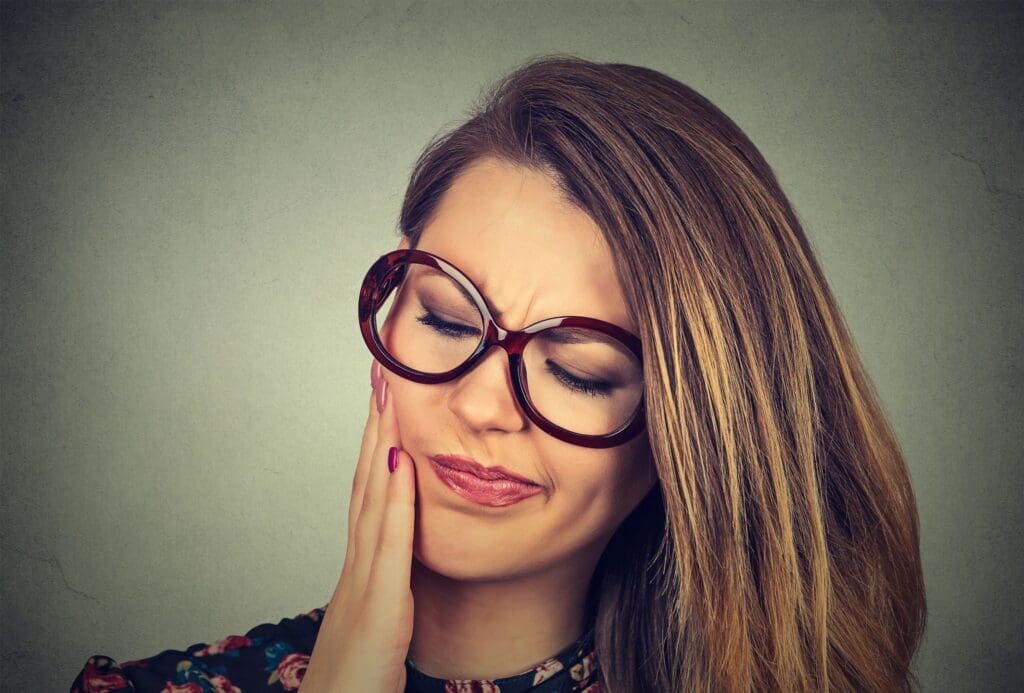 Woman with glasses experiencing toothache.
