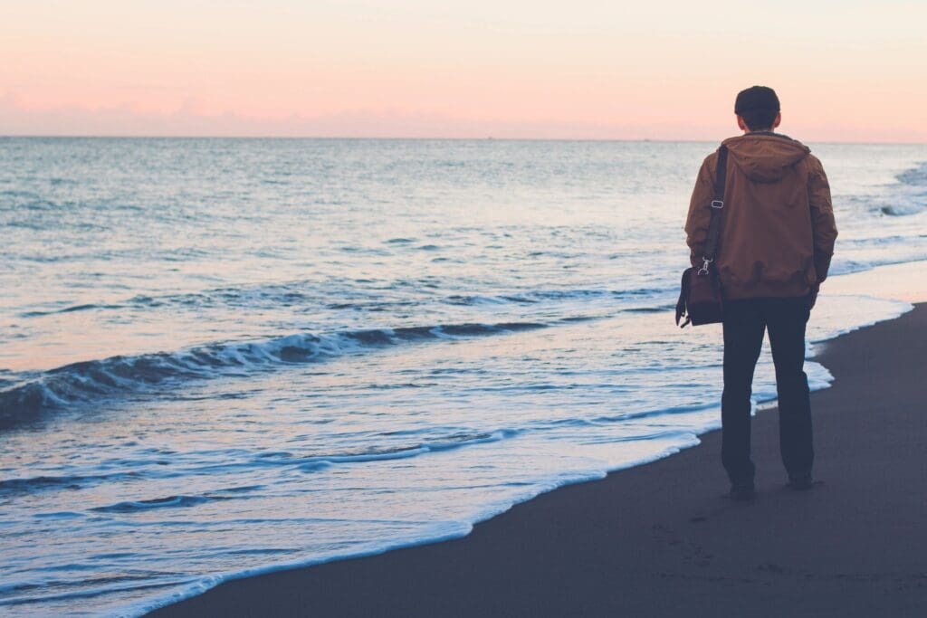 Man with bag on beach at sunset.