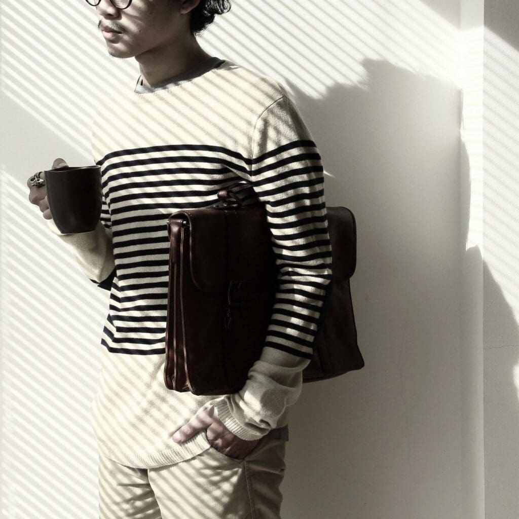 Man holding coffee, briefcase, striped sweater.