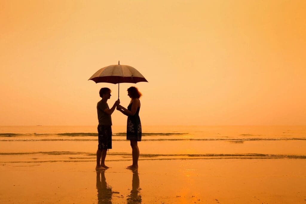 Silhouette couple sharing umbrella on beach.