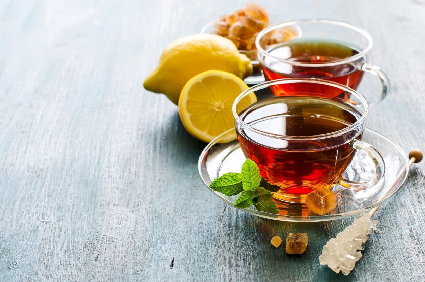 Two cups of tea with lemon and ginger on a table.